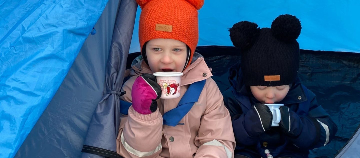 kaksi lasta juomassa mukeista teltassa